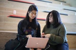 Two screenwriting students sitting on steps and looking at a laptop